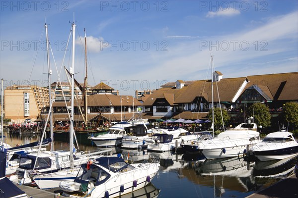 Port Solent Boats moored in the marina with people sitting at restaurant tables beyond beside a pub and housing apartments. Photo : Paul Seheult