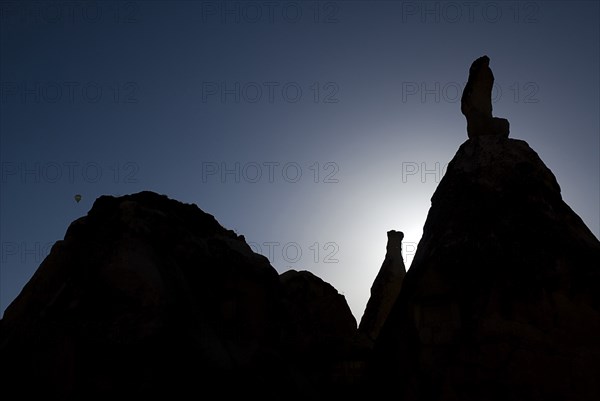 Distant hot air balloon in flight over silhouetted landscape of eroded rock forms. Photo : Hugh Rooney