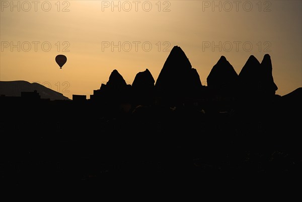Distant hot air balloon in flight over silhouetted landscape of eroded rock forms. Photo : Hugh Rooney