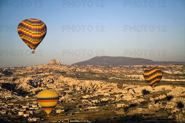 Hot air balloons in flight over landscape in early morning sunlight with Uchisar town in background.. Photo: Hugh Rooney