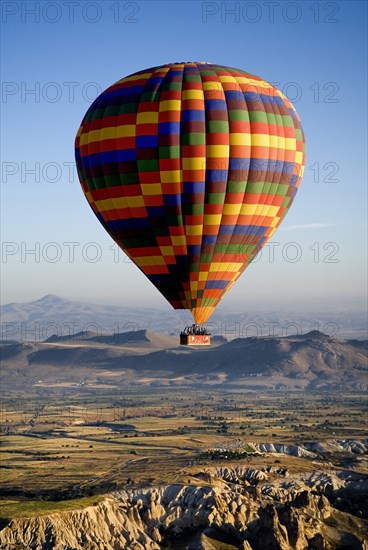 Brightly coloured hot air balloon in flight over the landscape in early morning sunshine. Photo : Hugh Rooney