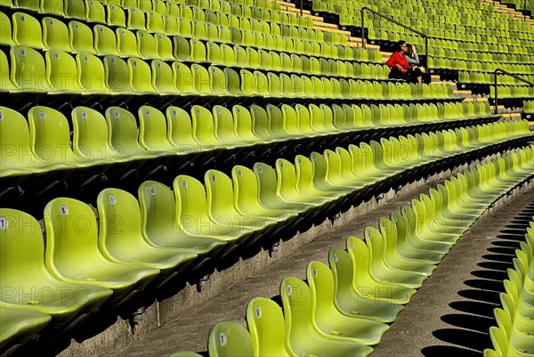 Olympic Stadium. Curved section of bright green seating in the stadium with couple seated at far end. Photo : Hugh Rooney