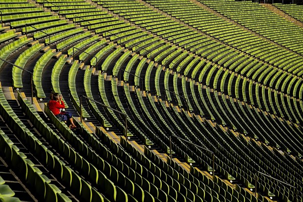 Olympic Stadium. Curved section of bright green seating in the stadium with seated figure centre left of image. Photo : Hugh Rooney