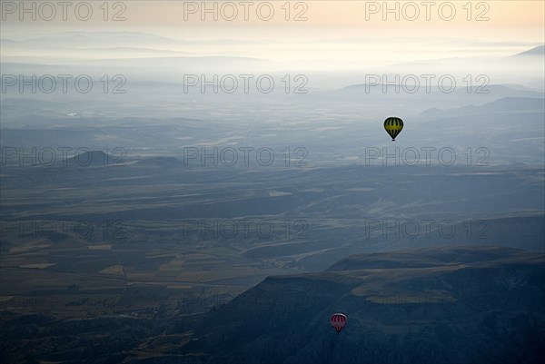 Hot air balloons in flight over landscape in misty early morning light with pale orange sky. Photo : Hugh Rooney