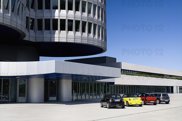 BMW Headquarters exterior. The BMW Tower which stands 101 metres tall and mimics the shape of tyres part view of tower base with minis parked in foreground. Photo : Hugh Rooney