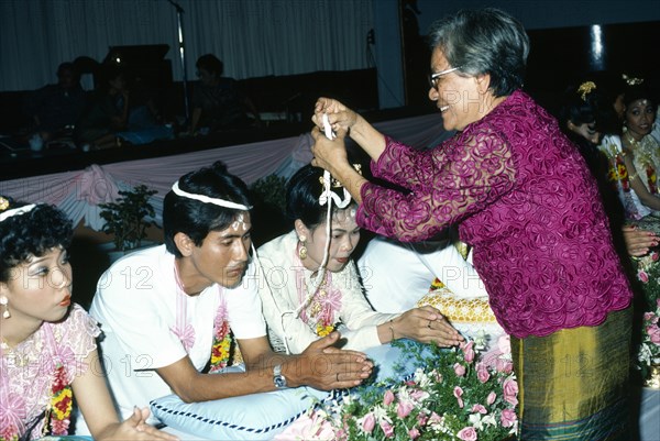 Couple being symbolically bound together with cotton at Thai Buddhist wedding ceremony. Photo : Nancy Durrell McKenna