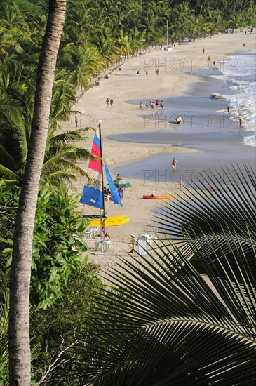 Mexico, Guerrero, Zihuatanejo, View onto Playa la Ropa with a colourful sailboat on sandy beach lined with palm trees. 
Photo : Nick Bonetti