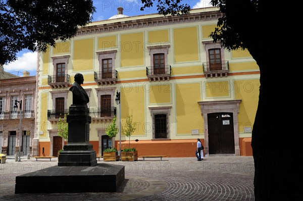 Mexico, Bajio, Zacatecas, Plaza San Augustin. Yellow painted building and statue. 
Photo : Nick Bonetti