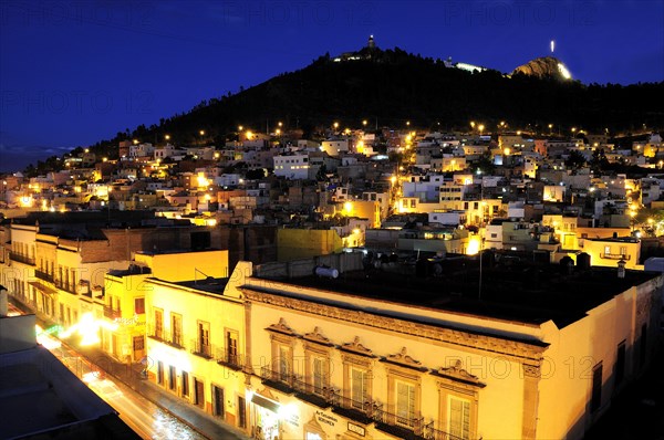 Mexico, Bajio, Zacatecas, View across city rootftops illuminated at night towards Cerro de la Buffa. 
Photo : Nick Bonetti