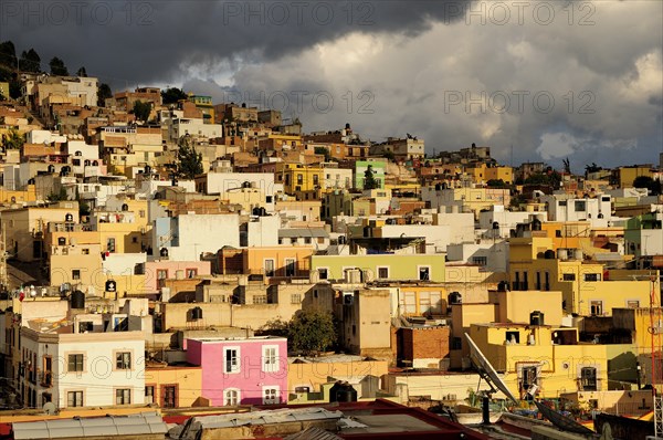 Mexico, Bajio, Zacatecas, Colourful houses clinging to the hillside below sky of thick grey cloud. 
Photo : Nick Bonetti