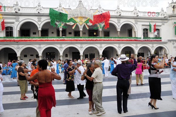 Mexico, Veracruz, Veracruz, Couples dancing in the Zocalo with facade of government buildings behind hung with bright decorations in the national colours for Independence Day celebrations. 
Photo : Nick Bonetti