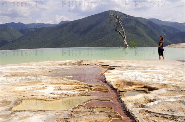 Mexico, Oaxaca, Hierve el Agua, Female tourist standing in limestone pool with view towards mountainous landscape densely covered with trees. 
Photo : Nick Bonetti
