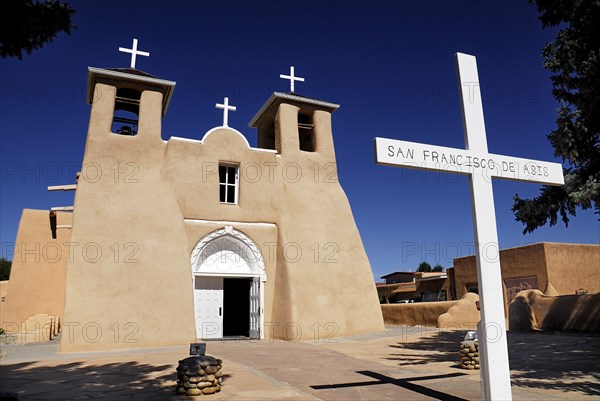 USA, New Mexico, Taos, Church of San Francisco de Asis. Adobe style church exterior with name on simple white painted cross in foreground. 
Photo : Hugh Rooney