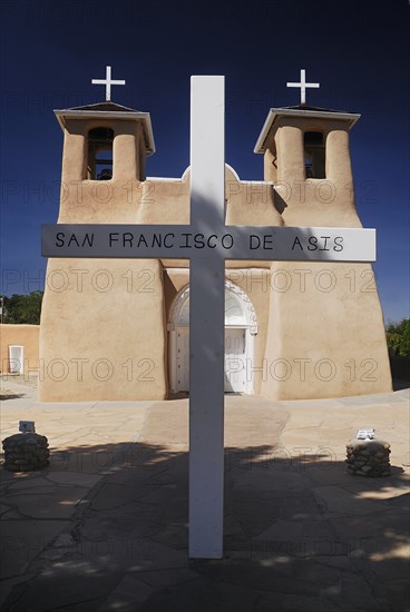 USA, New Mexico, Taos, Church of San Francisco de Asis. Adobe style church exterior with name on simple white painted cross in foreground. 
Photo : Hugh Rooney