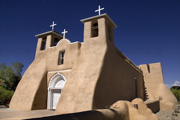 USA, New Mexico, Taos, Church of San Francisco de Asis. Angled view of adobe style exterior facade with white painted crosses on rooftop and bell towers. 
Photo : Hugh Rooney