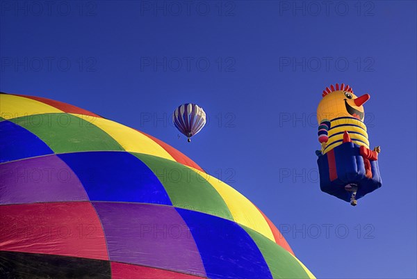 USA, New Mexico, Albuquerque, Annual balloon fiesta colourful hot air balloons ascending with part view of diamond check patterned top in foreground. 
Photo : Hugh Rooney