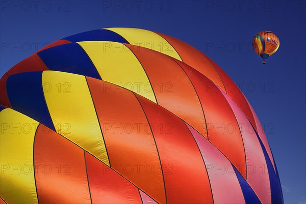 USA, New Mexico, Albuquerque, Annual balloon fiesta colourful hot air balloons with part view of red pink orange and yellow ribbed side of balloon being inflated in foreground. 
Photo : Hugh Rooney
