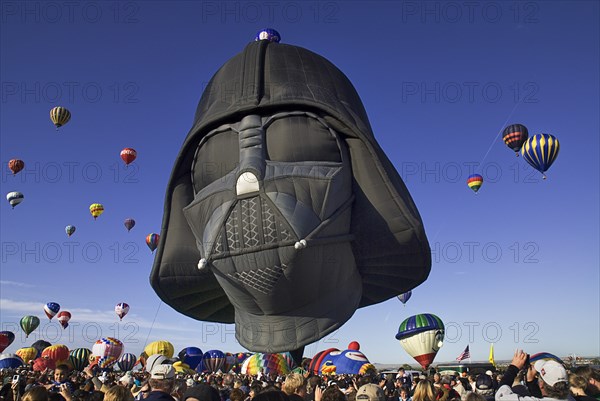 USA, New Mexico, Albuquerque, Annual balloon fiesta colourful hot air balloons in flight with darth vader shaped balloon above crowds in foreground. 
Photo : Hugh Rooney
