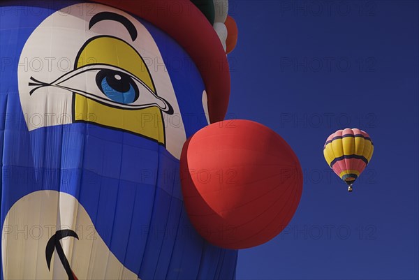 USA, New Mexico, Albuquerque, Annual balloon fiesta colourful hot air balloons in flight. Part view of balloon with the face of a clown in the foreground. 
Photo : Hugh Rooney