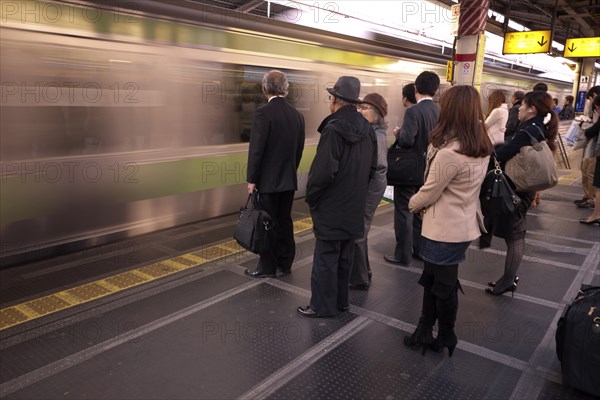 Japan, Honshu, Tokyo, Commuters waiting on platform whilst train speeds through without stopping. 
Photo : Jon Burbank