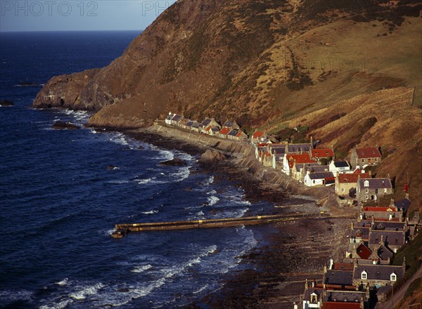 Scotland, Aberdeenshire, Crovie, One time fishing village seen from cliff top. Row of cottages at foot of steep hillside overlooking coast and stone jetty. 
Photo : Bryan Pickering