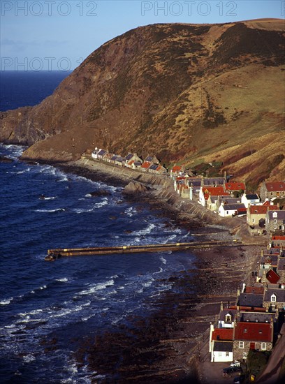 Scotland, Aberdeenshire, Crovie, One time fishing village seen from cliff top. Row of cottages at foot of steep hillside overlooking coast and stone jetty. 
Photo : Bryan Pickering