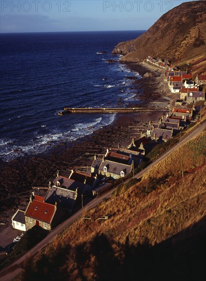 Scotland, Aberdeenshire, Crovie, One time fishing village seen from cliff top. Row of cottages at foot of steep hillside overlooking coast and stone jetty. 
Photo : Bryan Pickering