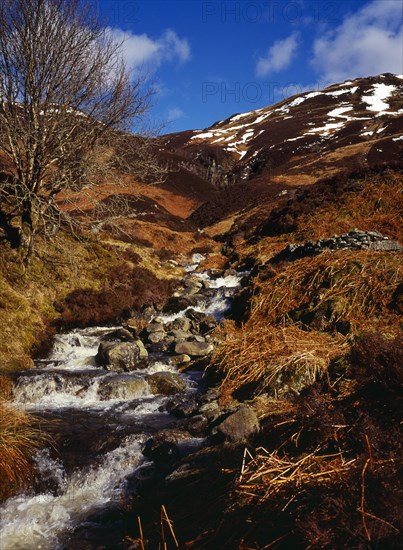 Scotland, Argyll and Bute, Loch Lubnaig, Loch Lomand and Trossachs National Park. Mountain stream flows from west side of Benn Each south of Loch Earn. Patches of snow on mountainside beyond. 
Photo : Bryan Pickering