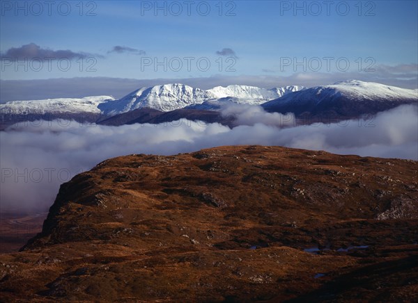 Scotland, Highlands, West, Ben More Forest and snow covered Assynt Mountains 998 metres at highest point above thick white cloud on skyline. View from Knockan Crag. 
Photo : Bryan Pickering