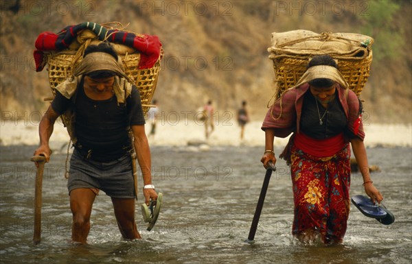Nepal, East, Arun River Valley, Porters carrying laden baskets fording the Piluwa Khola river. 
Photo : Chris Beall