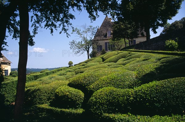 France, Aquitaine, Dordogne, Chateau de Marqueyssac near Vezac. Exterior and gardens with clipped boxwood hedges and topiary. Part framed by trees in foreground. 
Photo : Mike Southern