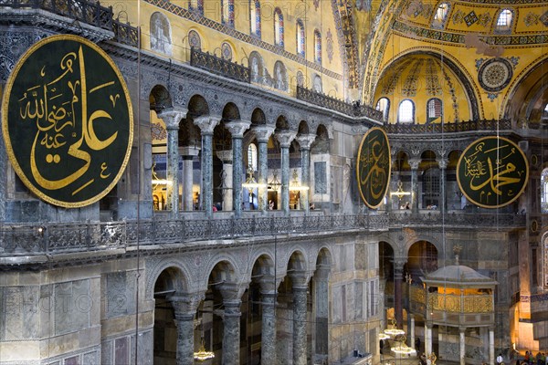 Turkey, Istanbul, Sultanahmet Haghia Sophia North Gallery beside the Nave with sightseeing tourists and Arab Muslim text on calligraphic roundels on the walls with the Lodge of The Sultan below. 
Photo : Paul Seheult