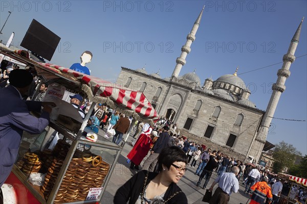 Turkey, Istanbul, Eminonu Yeni Camii New Mosque with pretzel vendor in the square. 
Photo : Stephen Rafferty