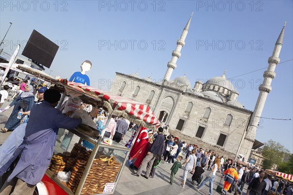 Turkey, Istanbul, Eminonu Yeni Camii New Mosque with pretzel vendor in the square. 
Photo : Stephen Rafferty
