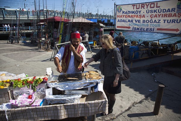 Turkey, Istanbul, Karakoy Galata fish market man selling freshly grilled fish served in a bread roll whilst talking on a mobile phone. 
Photo : Stephen Rafferty