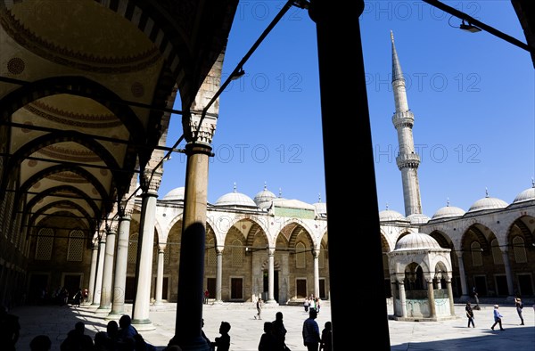 Turkey, Istanbul, Sultanahmet Camii The Blue Mosque Courtyard and minaret with Absolutions Fountain in the middle and tourists walking in the shade under domed arches. 
Photo : Paul Seheult