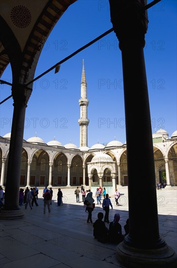 Turkey, Istanbul, Sultanahmet Camii The Blue Mosque Courtyard and minaret with Absolutions Fountain in the middle and tourists walking in the shade under domed arches. 
Photo : Paul Seheult