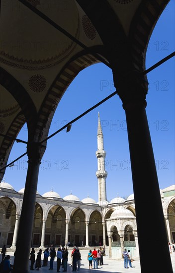 Turkey, Istanbul, Sultanahmet Camii The Blue Mosque Courtyard and minaret with Absolutions Fountain in the middle and tourists walking in the shade under domed arches. 
Photo : Paul Seheult