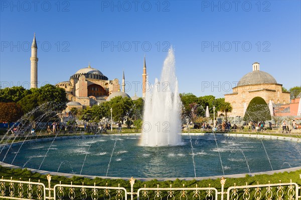 Turkey, Istanbul, Sultanahmet Haghia Sophia with dome and minarets beyond the water fountain and Baths of Roxelana in the gardens with sightseeing tourists. 
Photo : Paul Seheult