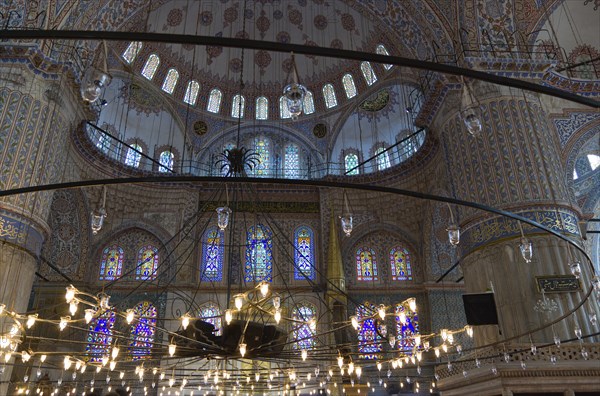 Turkey, Istanbul, Sultanahmet Camii The Blue Mosque interior with decorated painted domes with chandelier below and stained glass windows beyond. 
Photo : Paul Seheult