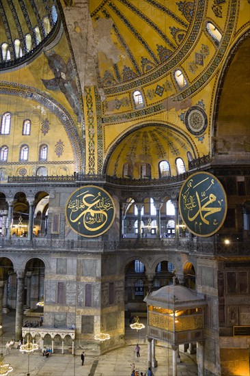 Turkey, Istanbul, Sultanahmet Haghia Sophia Sightseeing tourists beneath the dome with murals and chandeliers in the Nave of the Cathedral with calligraphic roundels of Arabic Koran texts above the Lodge of The Sultan. 
Photo : Paul Seheult