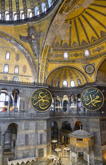 Turkey, Istanbul, Sultanahmet Haghia Sophia Sighseeing tourists beneath the dome with murals and chandeliers in the Nave of the Cathedral with calligraphic roundels of Arabic Koran texts abobe the Lodge of The Sultan. 
Photo : Paul Seheult