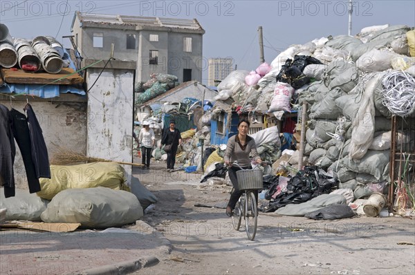 China, Jiangsu, Qidong, Female workers one on a bicycle leaving a recycling depot bundles of waste paper in plastic and polypropylene sacks. 
Photo : Trevor Page