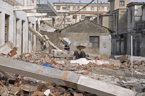 China, Jiangsu, Qidong, Female and male demolition workers in straw hats using hammers with flexible handles to demolish old residential buildings to make way for new construction. Trevor Page. 
Photo : Trevor Page