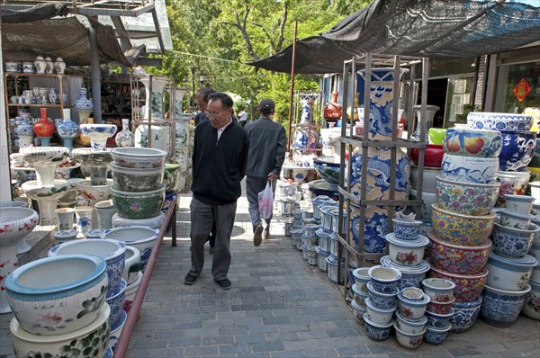 China, Jiangsu, Yangzhou, Ceramic pots for plants and decorative use in downtown canal-side street market. Man strolling through market looking at pots. Trees in background. Marco Polo once served as a municipal official of the city. Trevor Page. 
Photo : Trevor Page