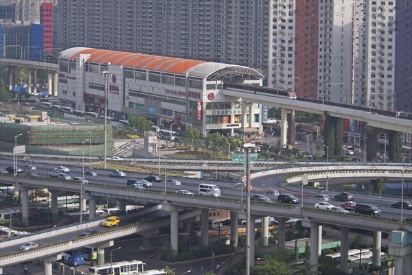 China, Shanghai, Light Railway train leaving Caoxi Road station in south Shanghai in the early morning with cars and buses at spaghetti junction Apartment blocks in background with windows forming a patern. 
Photo : Trevor Page