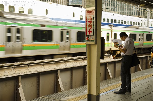 Japan, Honshu, Tokyo, Commuter on platform cooling himself with paper fan whilst waiting for his train. 
Photo : Jon Burbank