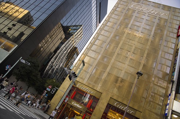 Japan, Honshu, Tokyo, Ginza Golden facade of the Cartier Building with the Chanel Building on left and DeBeers curved facade reflected in black glass on Chuo-dori Avenue. 
Photo : Jon Burbank