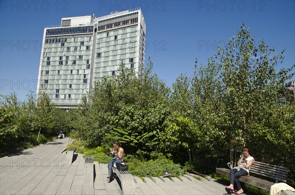 USA, New York, Manhattan, West Side High Line Park people realaxing along the benches around 13th street with the Standard Hotel in the background. 
Photo : Jon Burbank