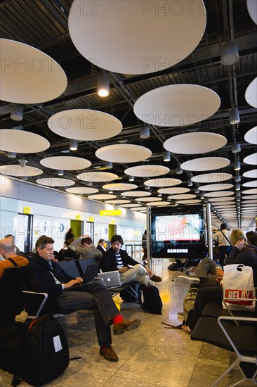 England, London, Heathrow Airport Terminal 5 disc ceiling in departures zone with passengers waiting in seating area at gate. 
Photo : Paul Seheult